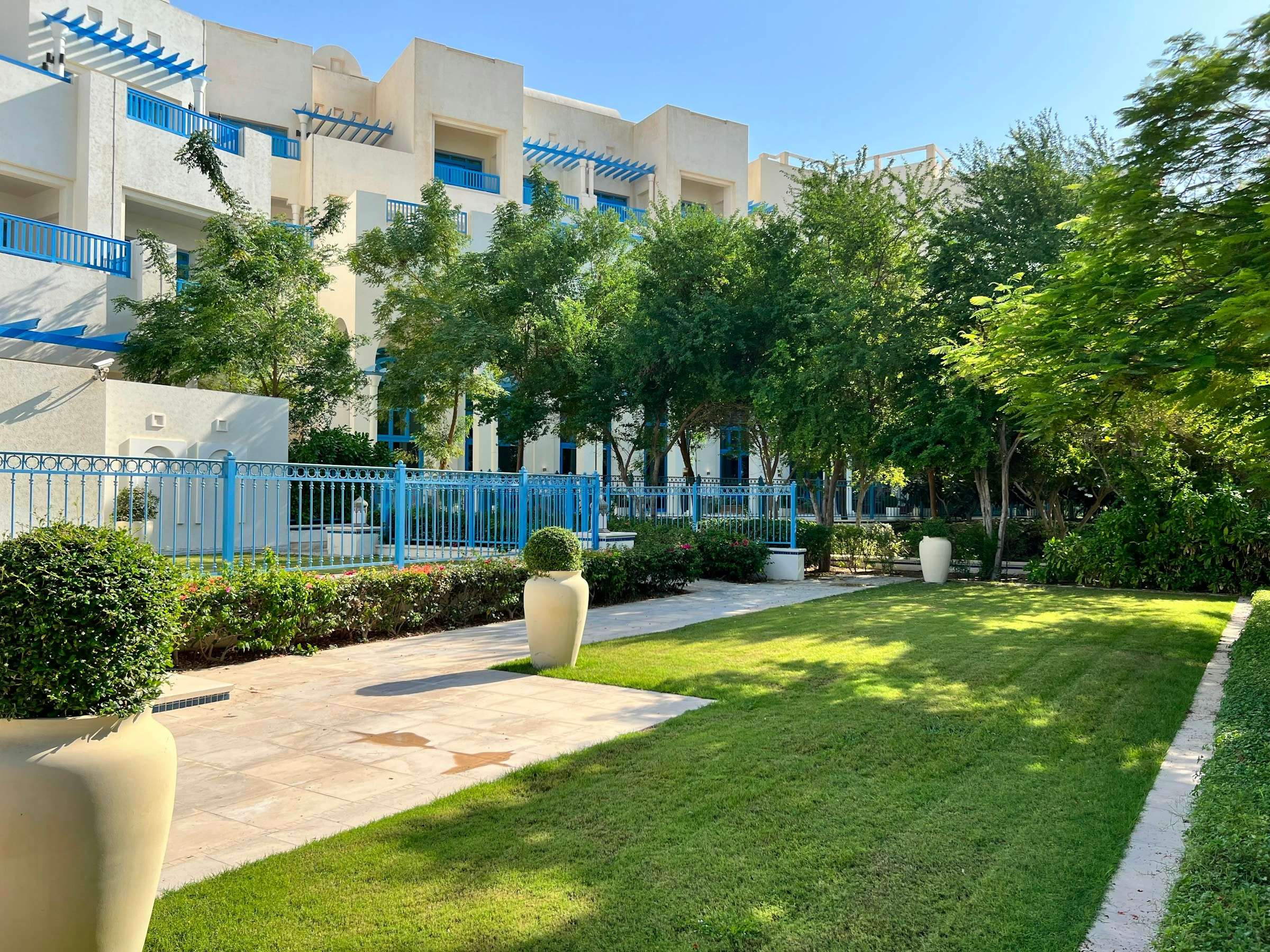 Zona ajardinada y cuidada de un conjunto residencial, con césped, setos y barandillas azules