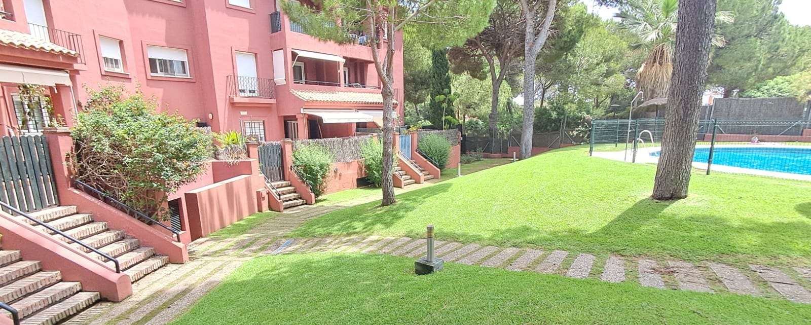 Jardín de una comunidad de viviendas con césped y piscina al fondo