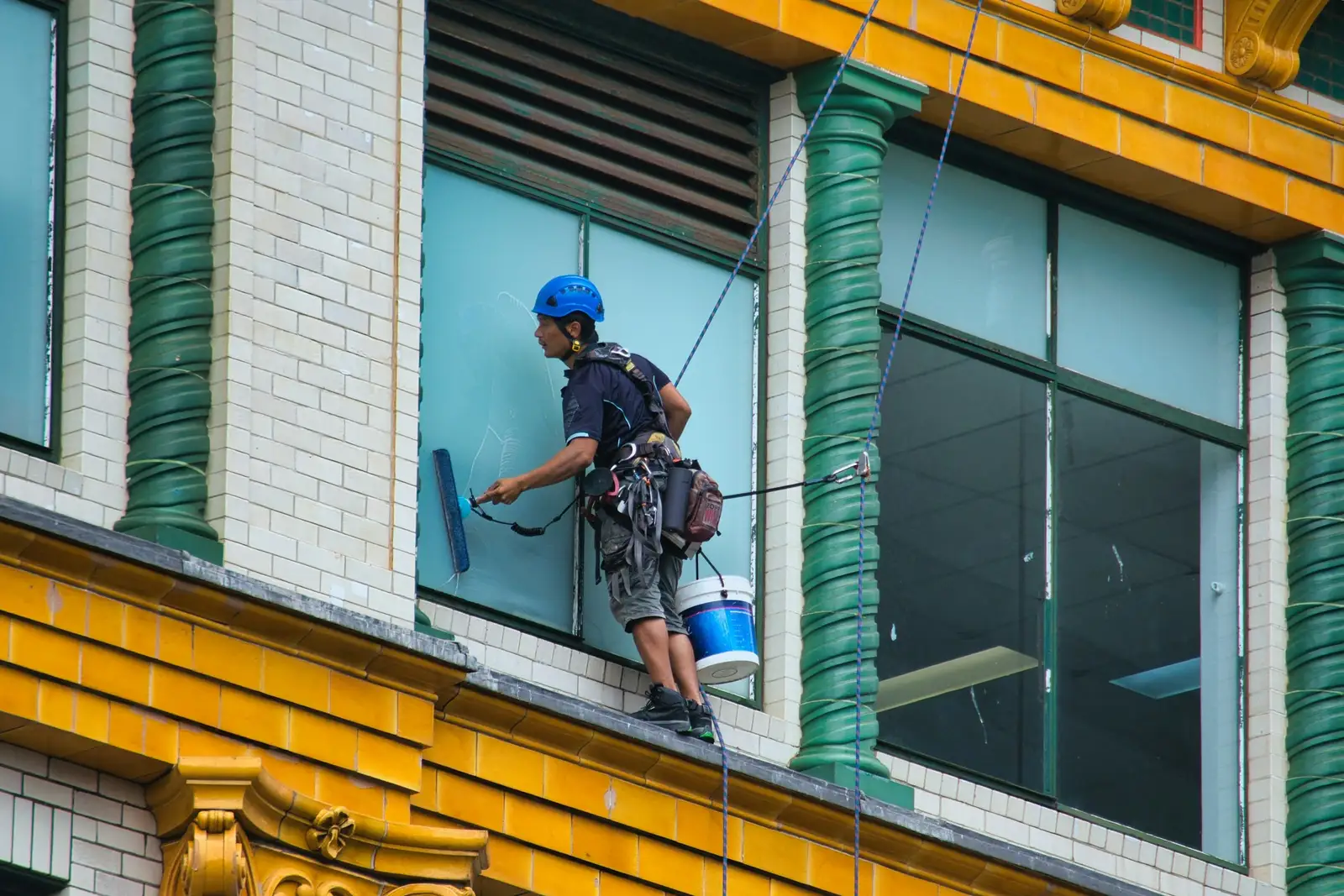 Operario asegurado con cuerdas limpiando un ventanal en fachada